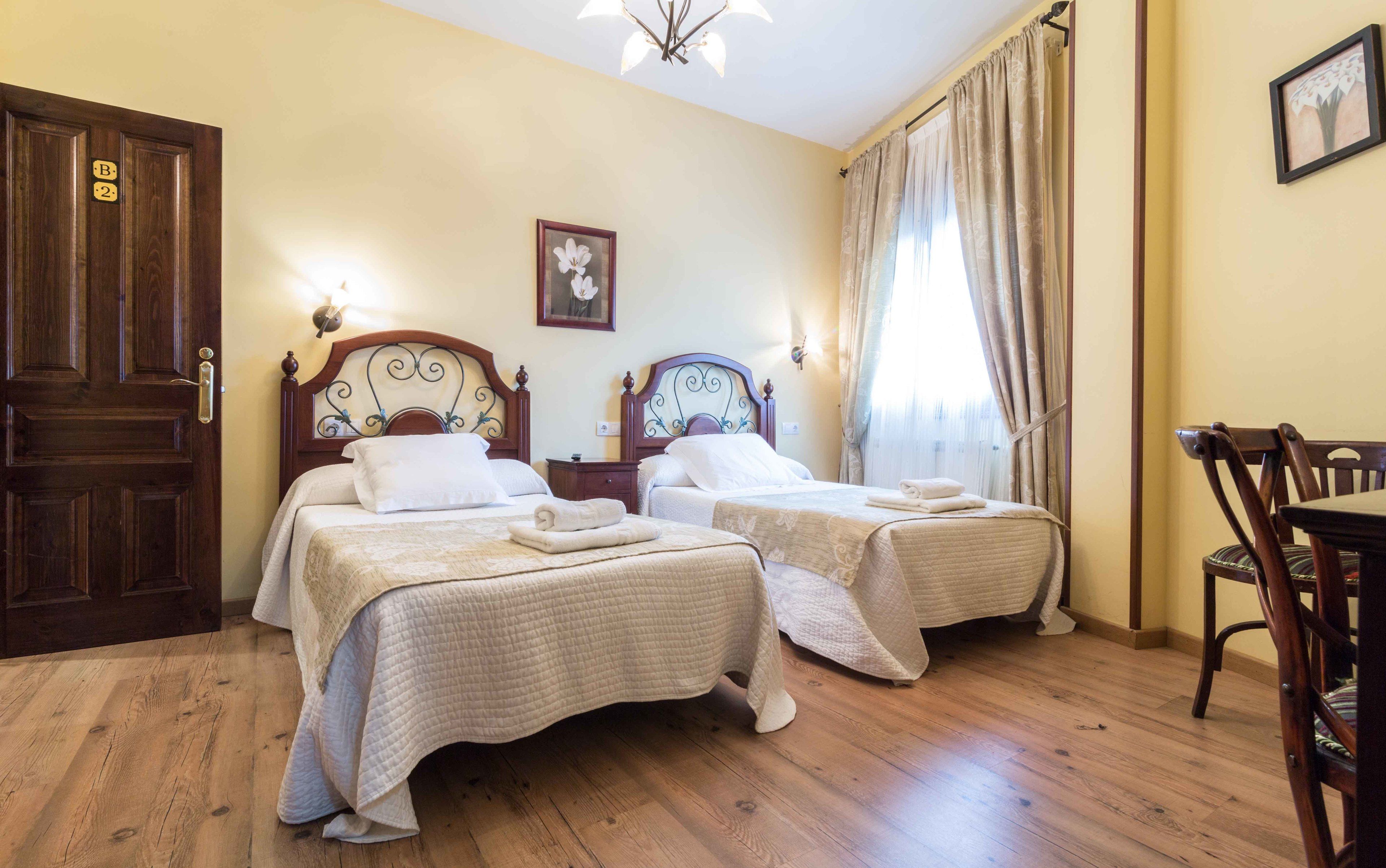 Habitación de hotel con dos camas, piso de madera, un candelabro y un área de comedor con una silla.