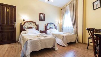 Habitación de hotel con dos camas, piso de madera, un candelabro y un área de comedor con una silla.