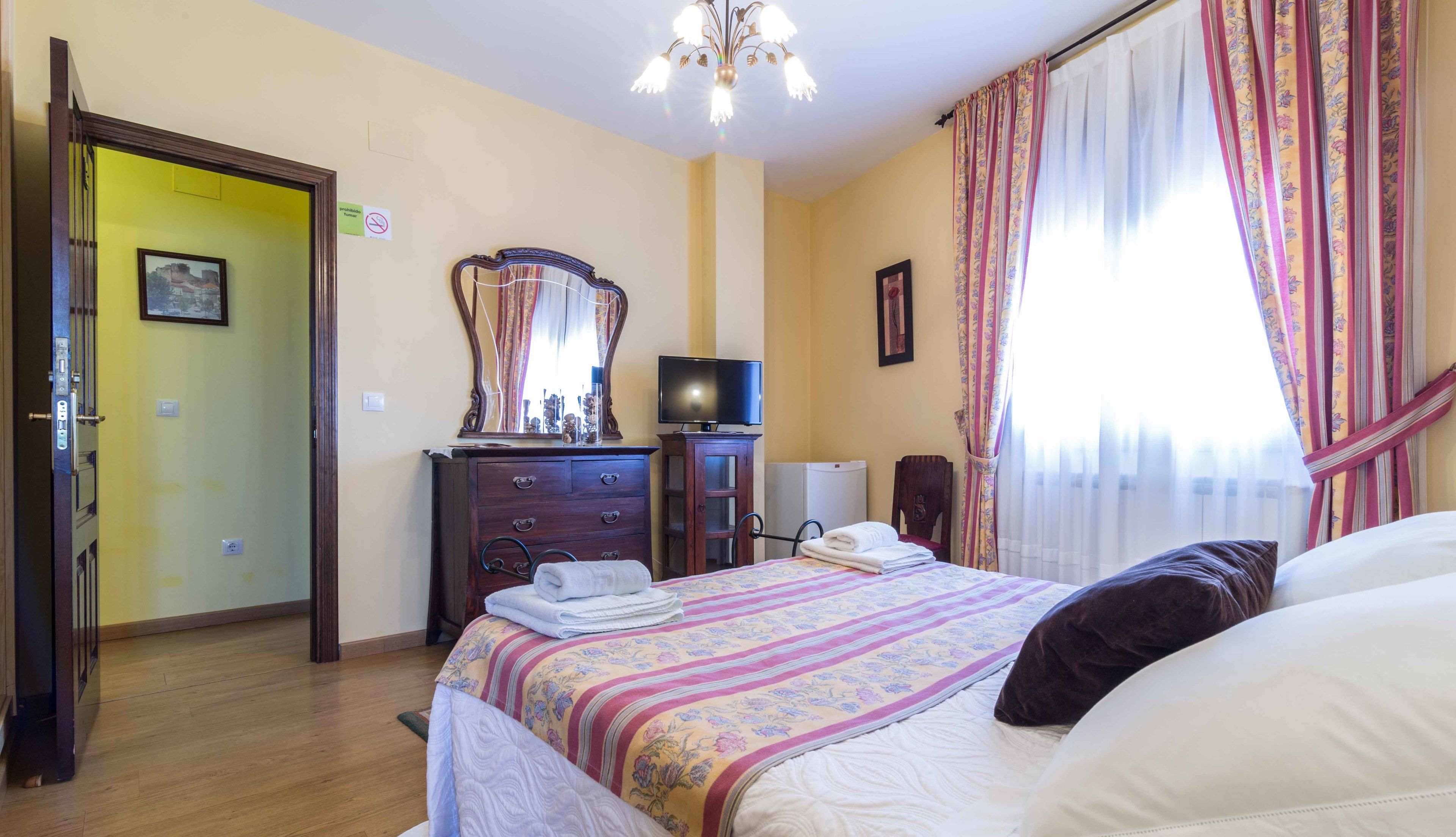 Una habitación de hotel con una cama, un tocador, un televisor y un espejo.