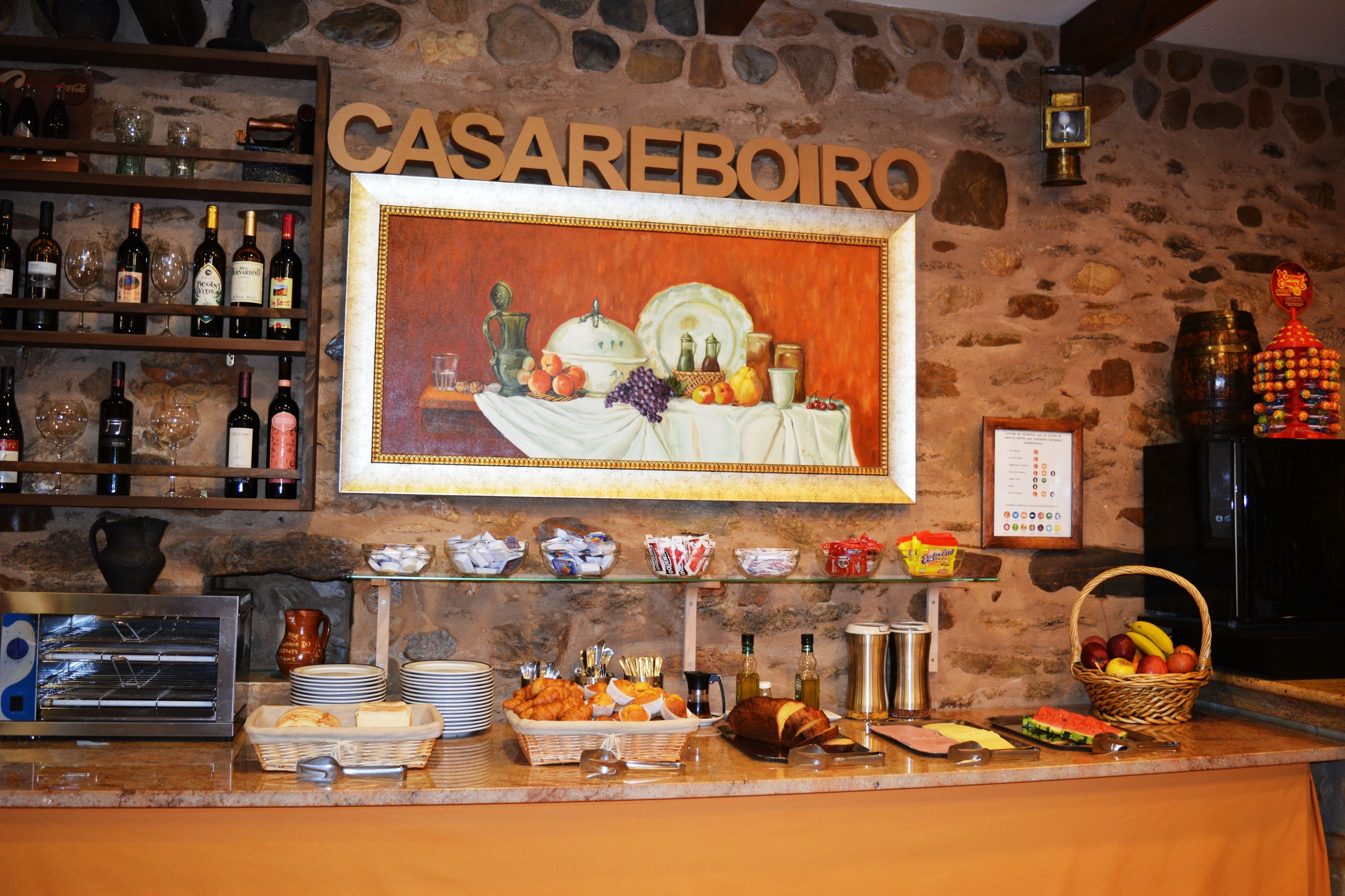 A breakfast buffet area with a variety of food items, a wine selection, and a large painting of a fruit and cheese display.