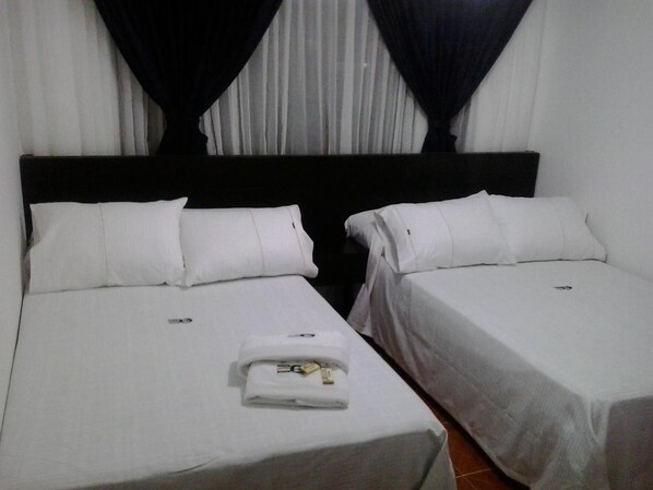 A hotel room with two single beds, white bedding, and a neatly folded towel on the left bed.