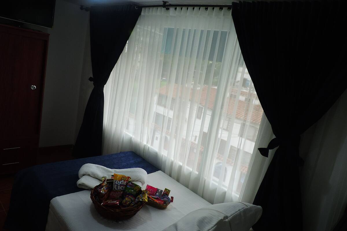 Une chambre d’hôtel avec un lit, une petite table avec des collations et une fenêtre avec des rideaux légers.