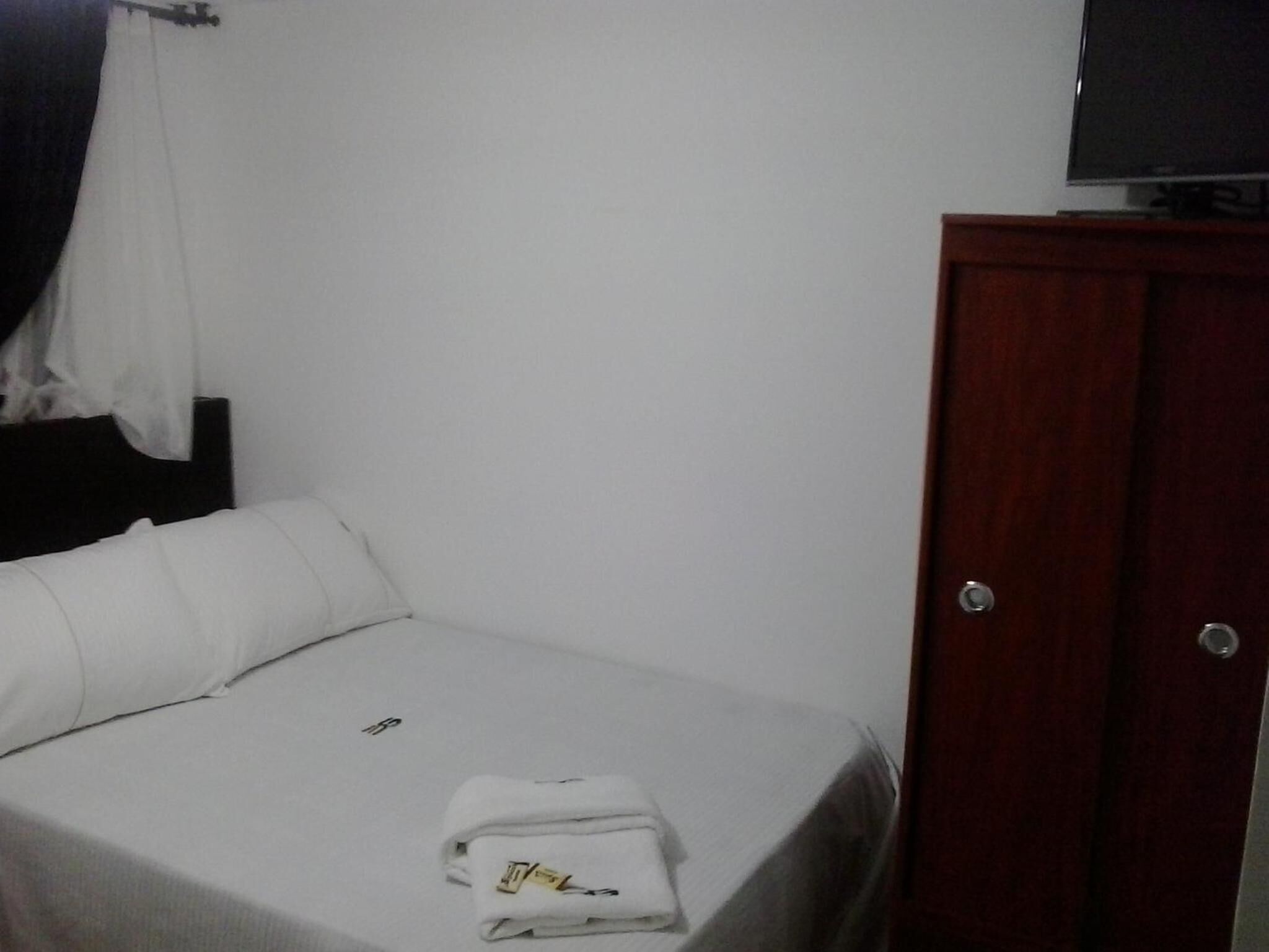 A small, single-bed room with a wooden wardrobe and a television on top.