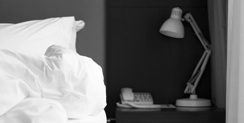A room with a bed, a nightstand with a lamp, and a telephone. The text 'Room assigned at Check-In' is visible.