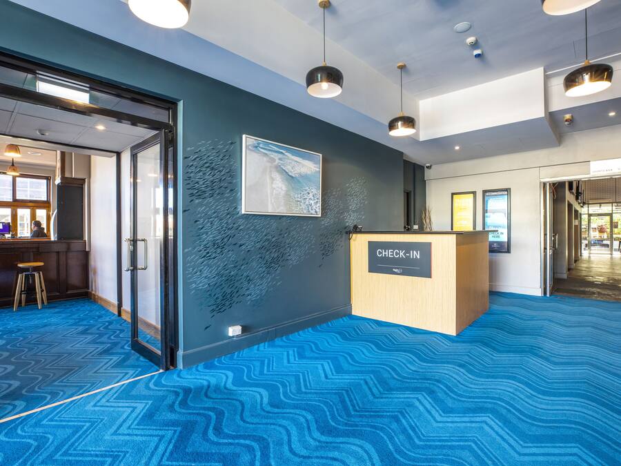 Un área de recepción con mostrador de check-in, un cuadro grande en la pared y una alfombra azul estampada.
