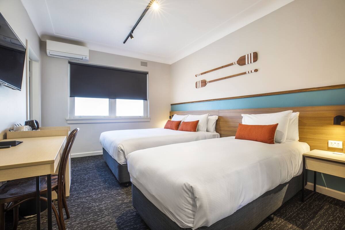 A hotel room with two beds, a desk, a chair, a TV, and a window.