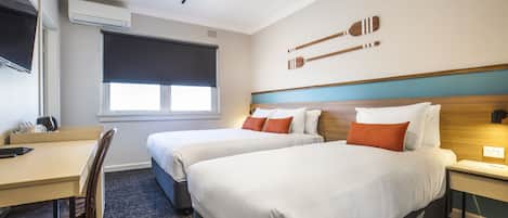 A hotel room with two beds, a desk, a chair, a TV, and a window.