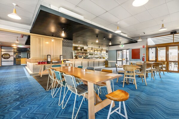 A modern conference room with a long table, chairs, and a bar area with shelves of bottles. - Nightcap at Ocean Beach Hotel (Umina Beach)