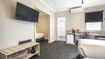 A hotel room with a bed, a desk, a chair, a TV, and a small kitchenette.