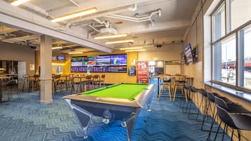 A pool table in a room with multiple screens, tables, and chairs.