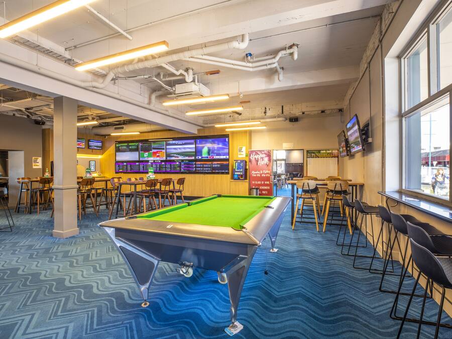A pool table in a room with multiple screens, tables, and chairs.