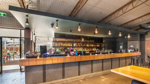 Zona de bar con una barra larga, estantes llenos de botellas y luces colgantes.