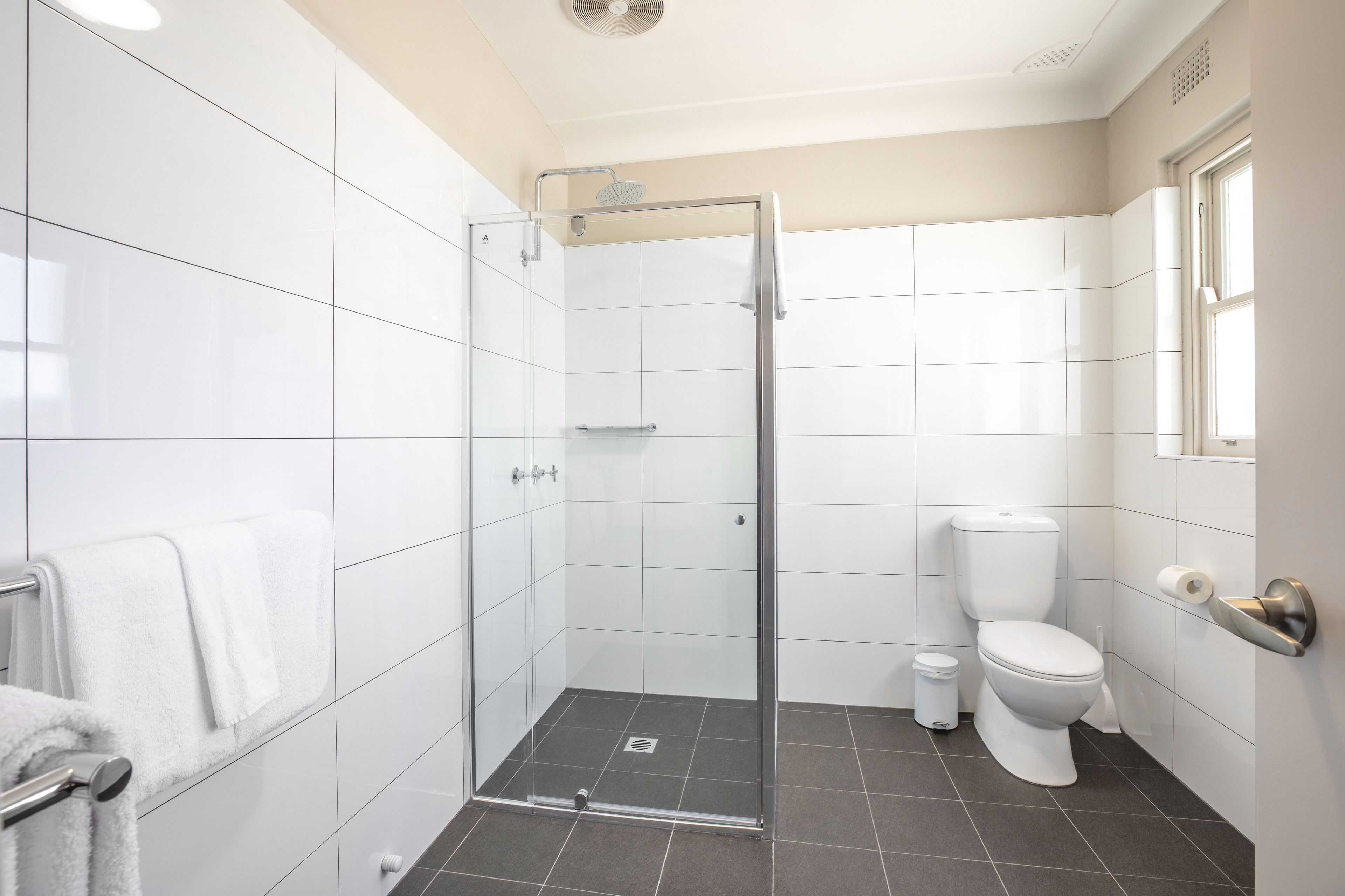 Een moderne badkamer met witte tegels, een glazen douchecabine, een toilet en een handdoekhouder.