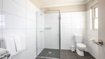Een moderne badkamer met witte tegels, een glazen douchecabine, een toilet en een handdoekhouder.