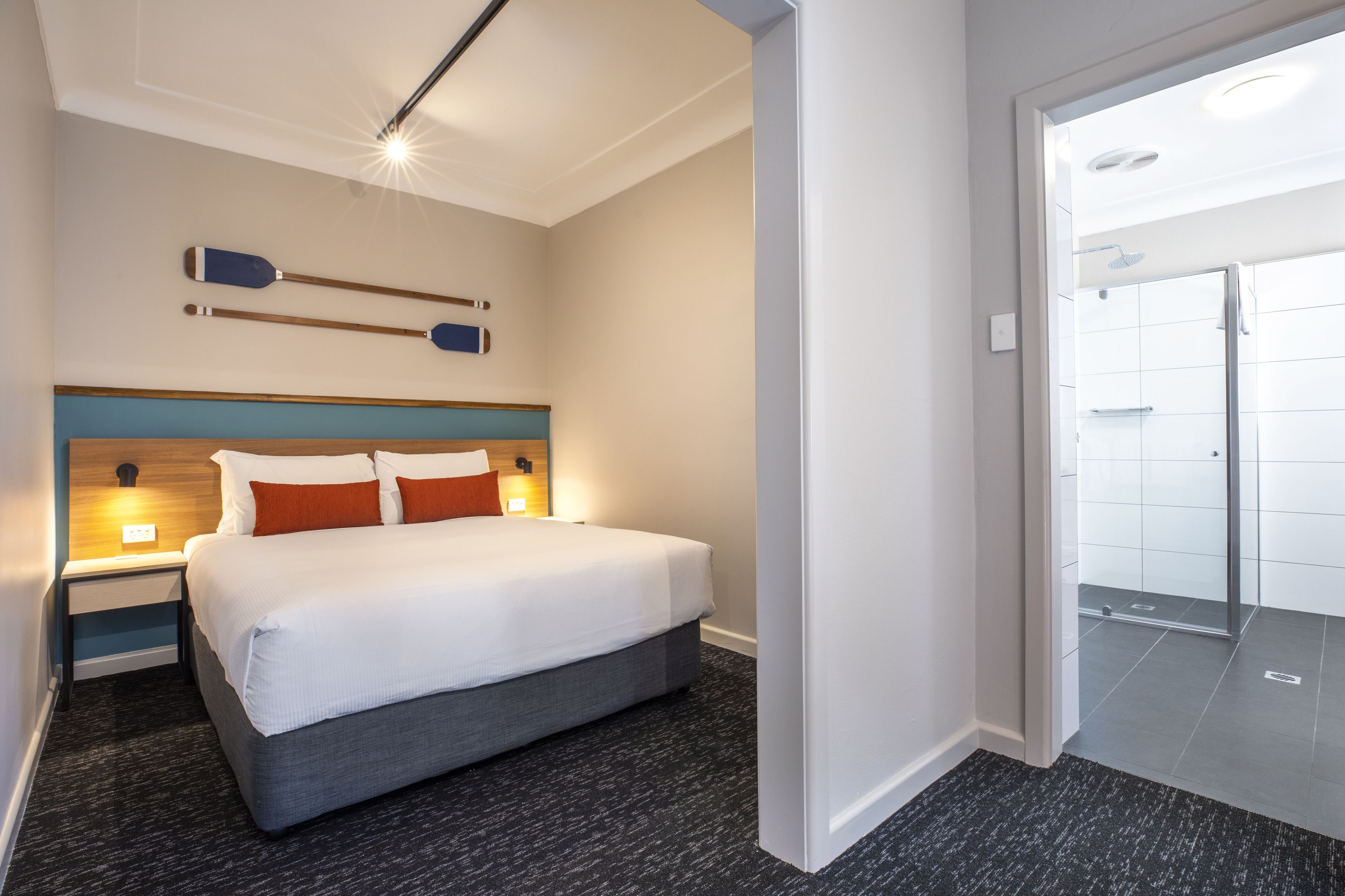 Una habitación de hotel moderna con una cama grande, un cabecero de madera y una mesita de noche con lámpara.
