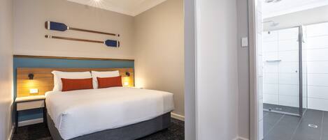 Una habitación de hotel moderna con una cama grande, un cabecero de madera y una mesita de noche con lámpara.