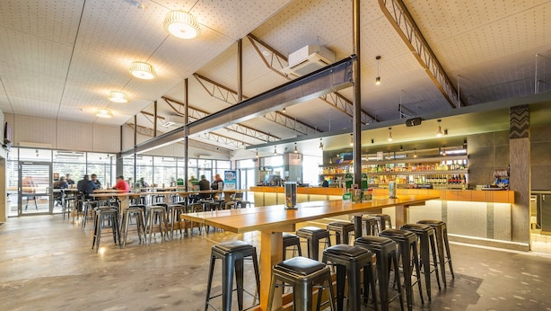 Un bar espacioso con taburetes altos, una barra alargada e iluminación industrial en el techo.
