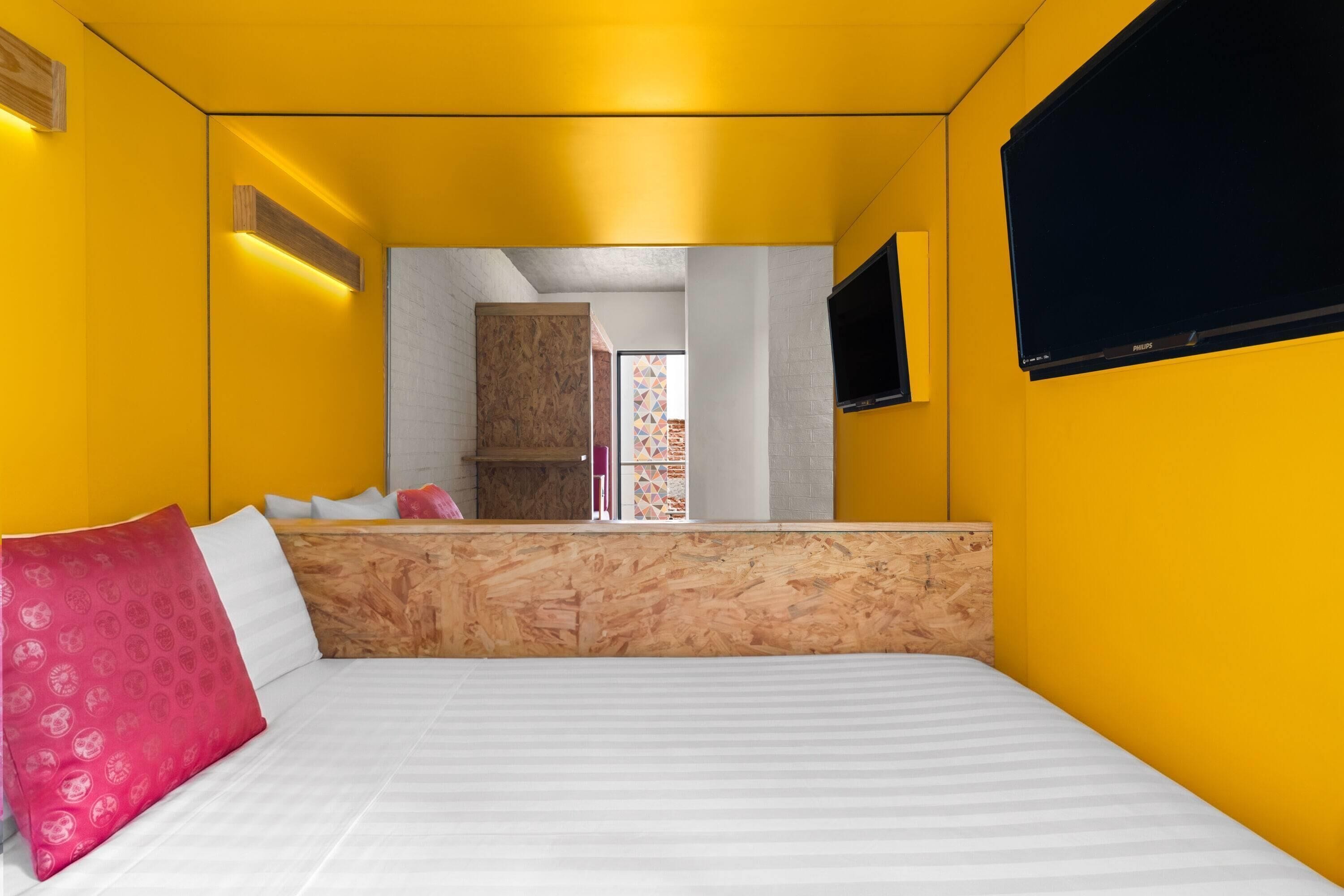 Une chambre avec un lit, une tête de lit en bois, un téléviseur et une vue sur un mur de briques et une porte.
