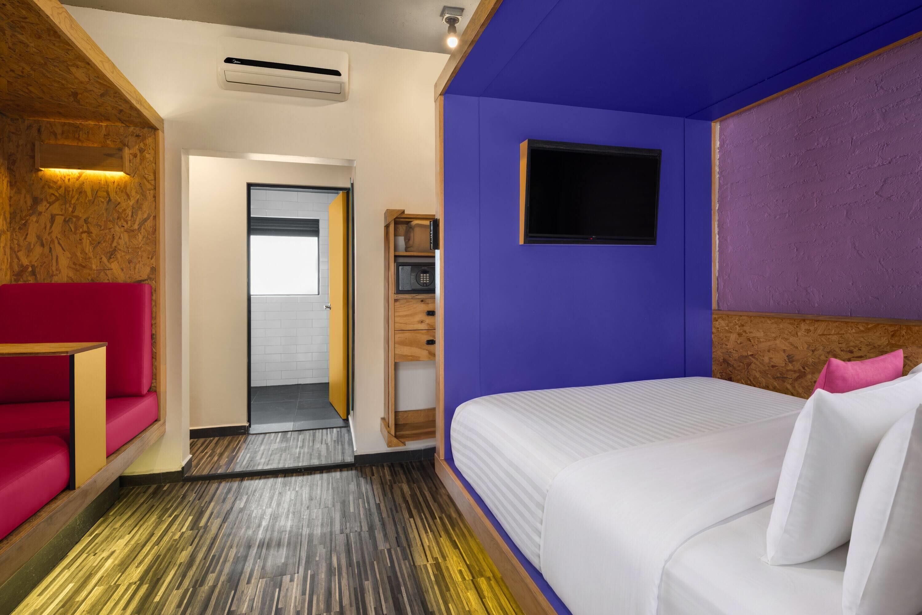 Habitació d'hotel amb llit, un sofà vermell, un armari de fusta i una petita televisió.