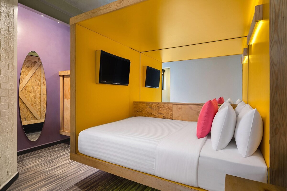 Une chambre d’hôtel avec un lit, une télévision, un miroir et une tête de lit en bois.