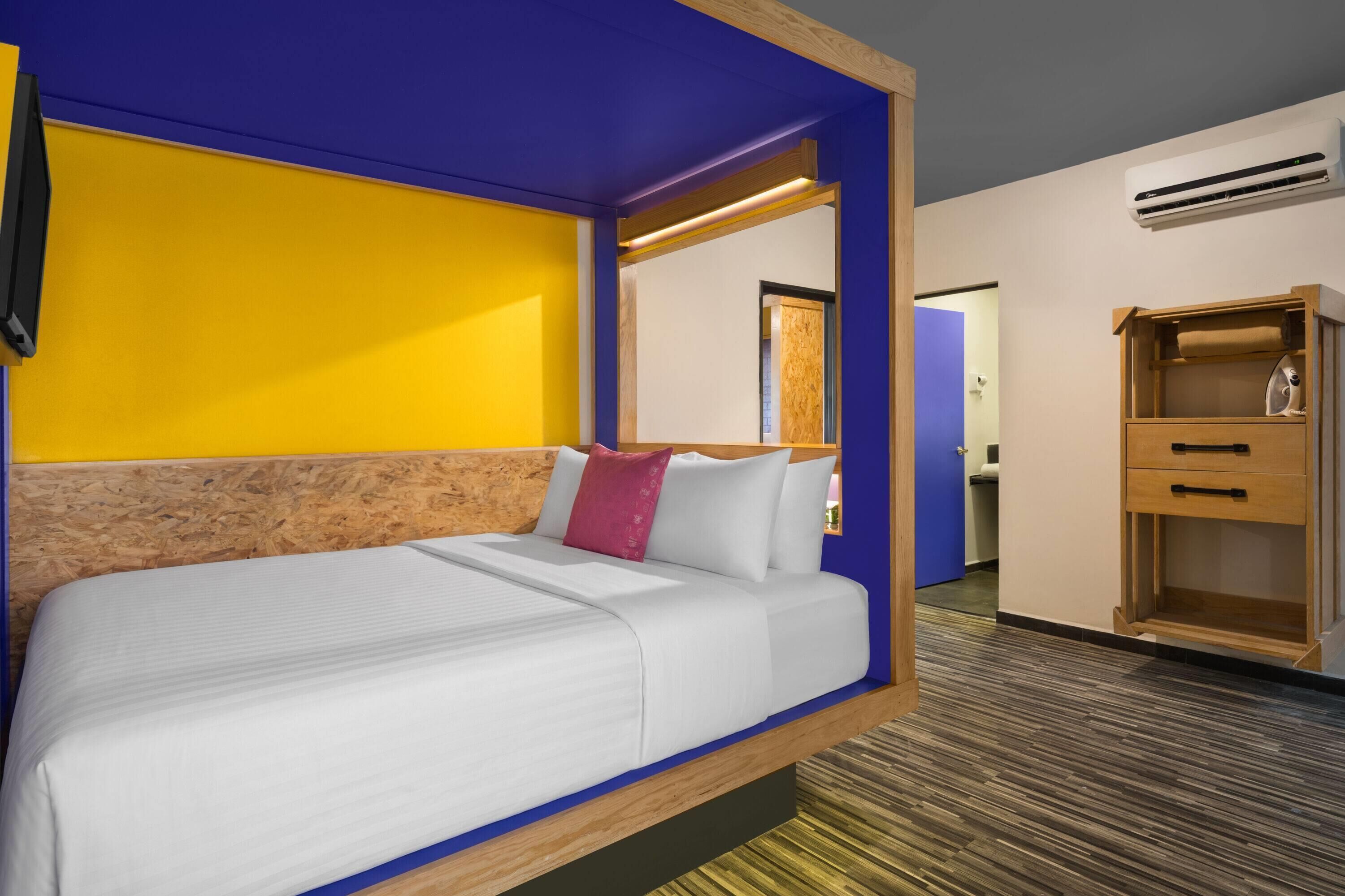 A hotel room with a bed, a wooden headboard, a wardrobe, and an air conditioning unit.