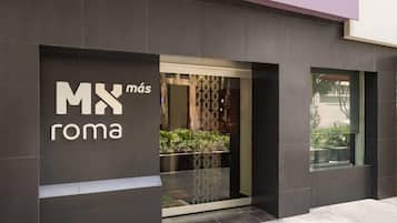 Fachada moderna de un edificio con una entrada grande y un letrero que dice 'MX más roma'.
