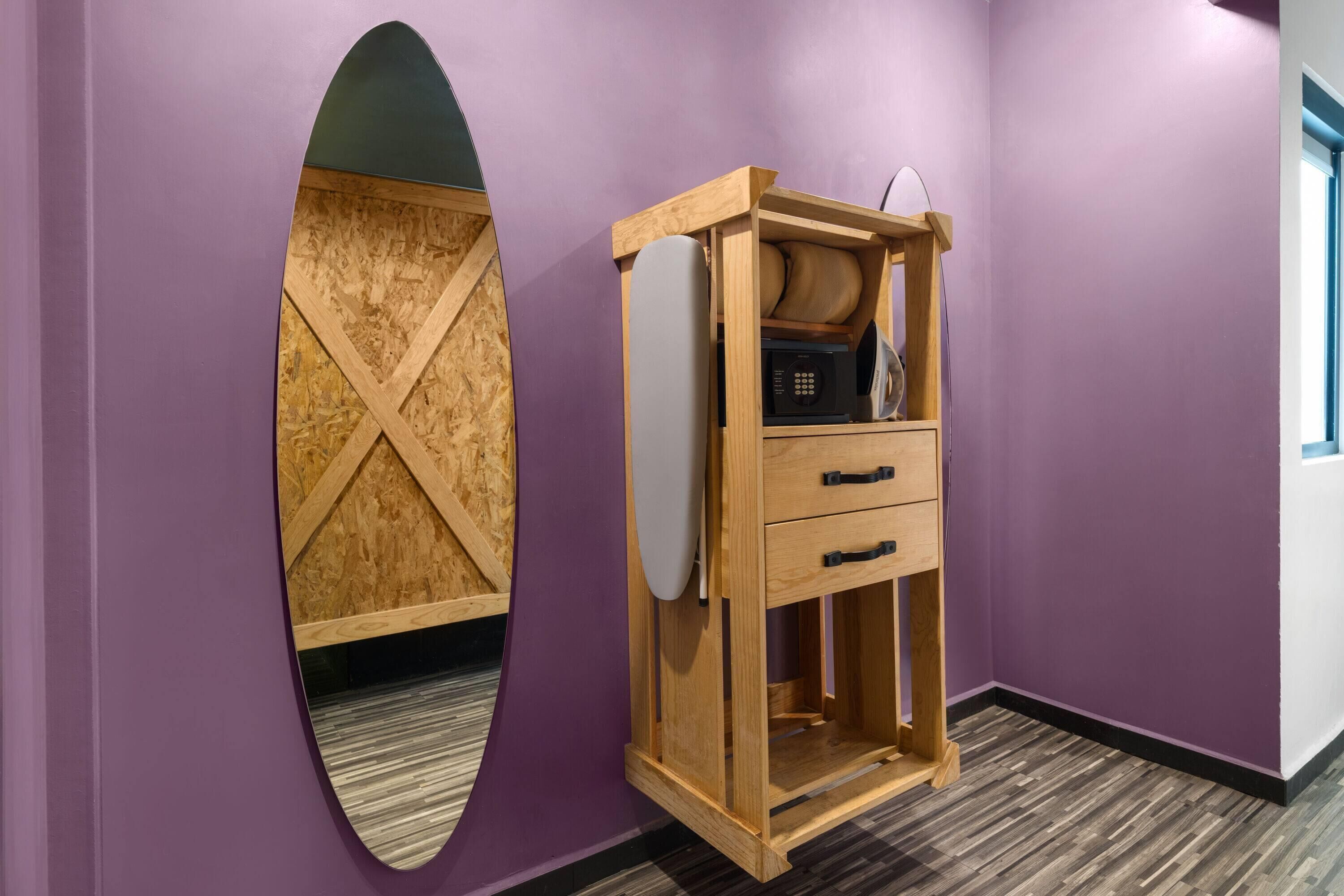 A room with a purple wall, a wooden cabinet with drawers, and a large mirror with a wooden frame.