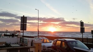 A sunset view from a balcony with a table and chairs, a car, and a railing overlooking the sea. - Rowntree Holiday Flats (Bridlington)