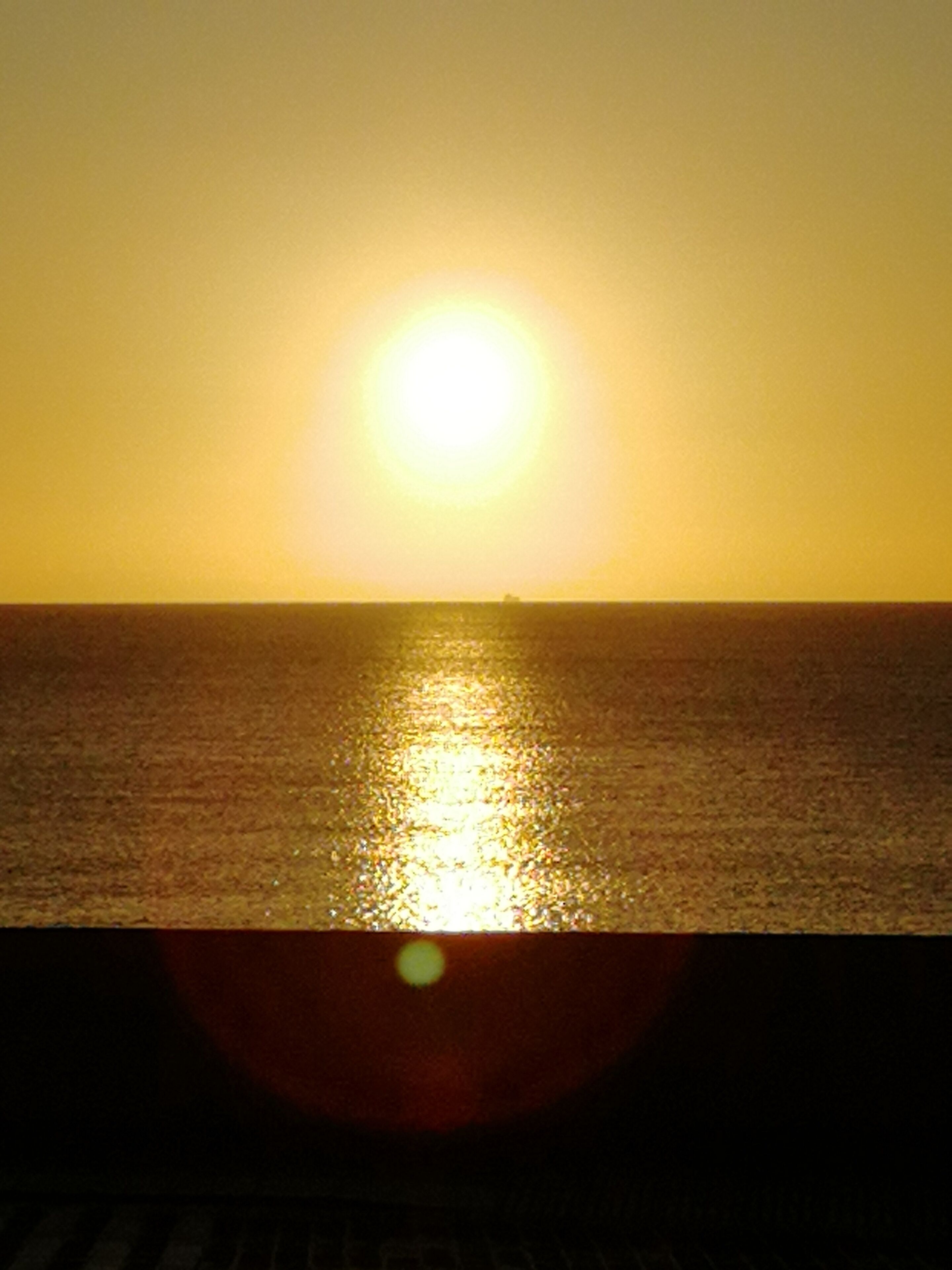 A sunset over a calm sea with a ship in the distance.