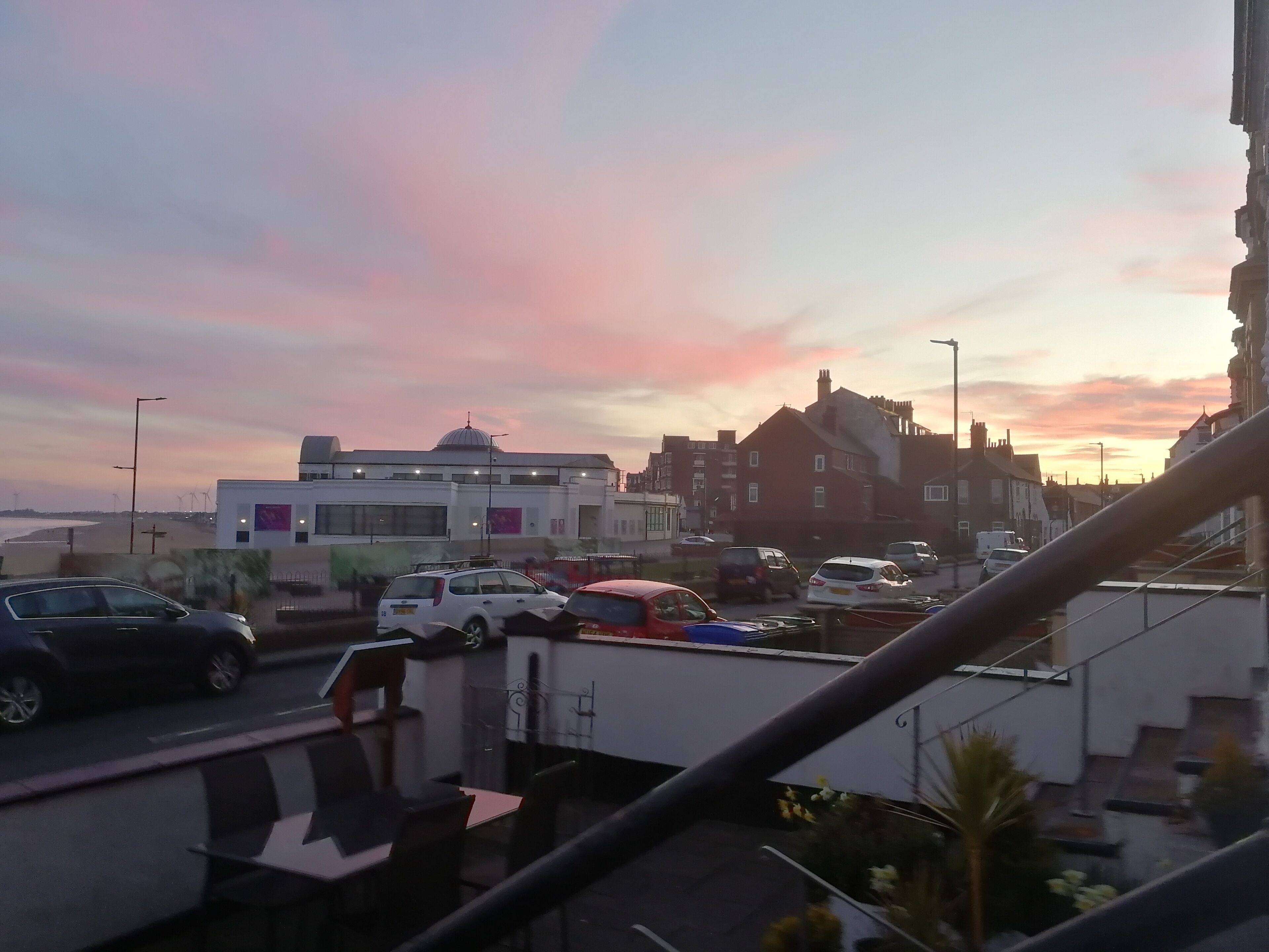 A parking area with several cars, a building with a dome, and a sunset in the background.