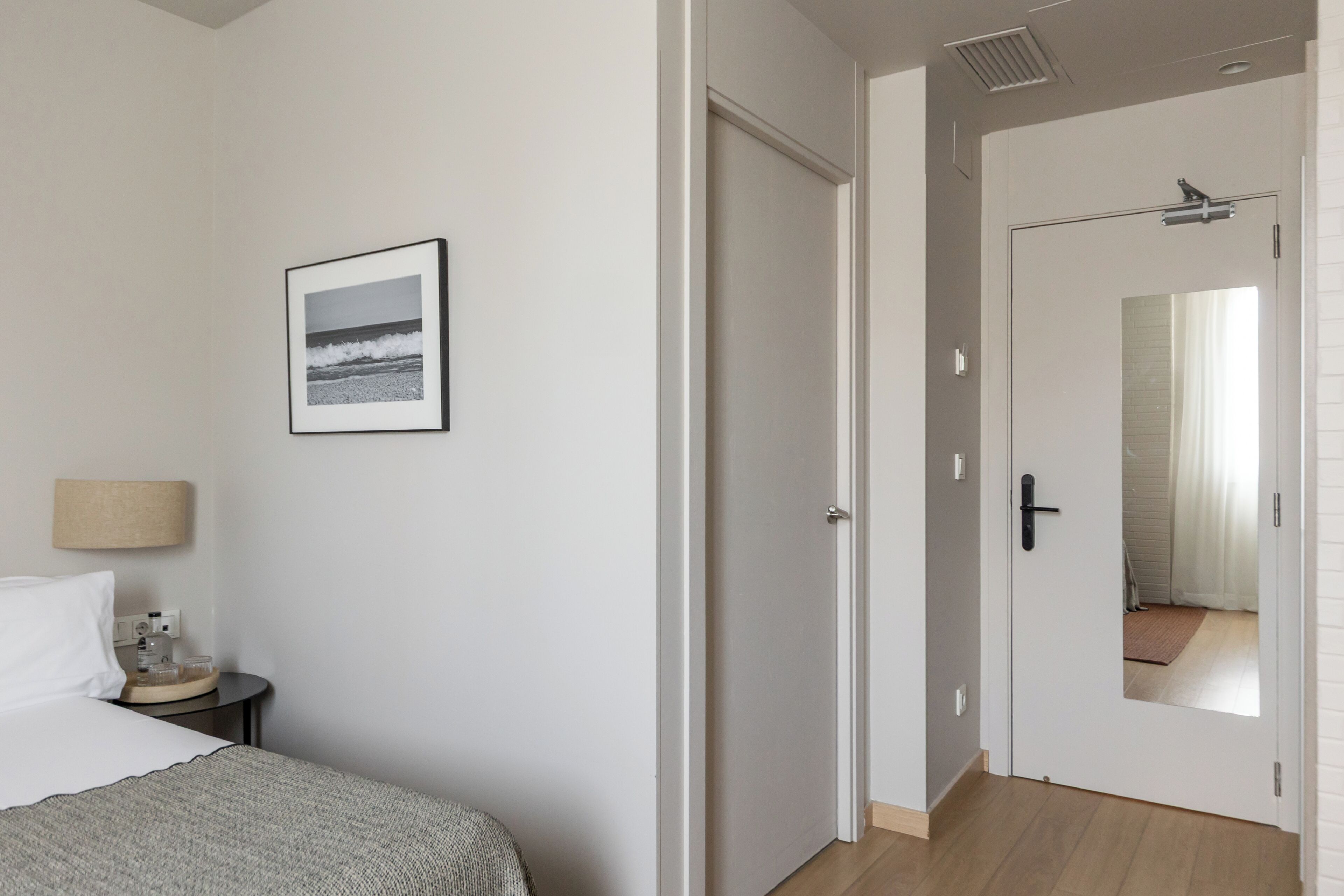 A hotel room with a bed, a bedside table with a lamp, a framed picture on the wall, and a door leading to a bathroom.