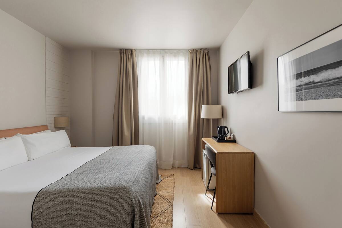 A hotel room with a bed, a desk, a lamp, a television, and a framed picture on the wall.