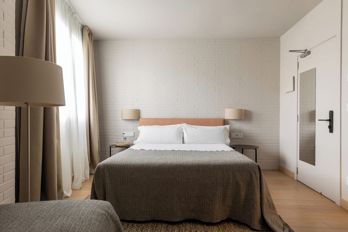 A hotel room with a bed, two bedside tables, a lamp, a mirror, and a door.