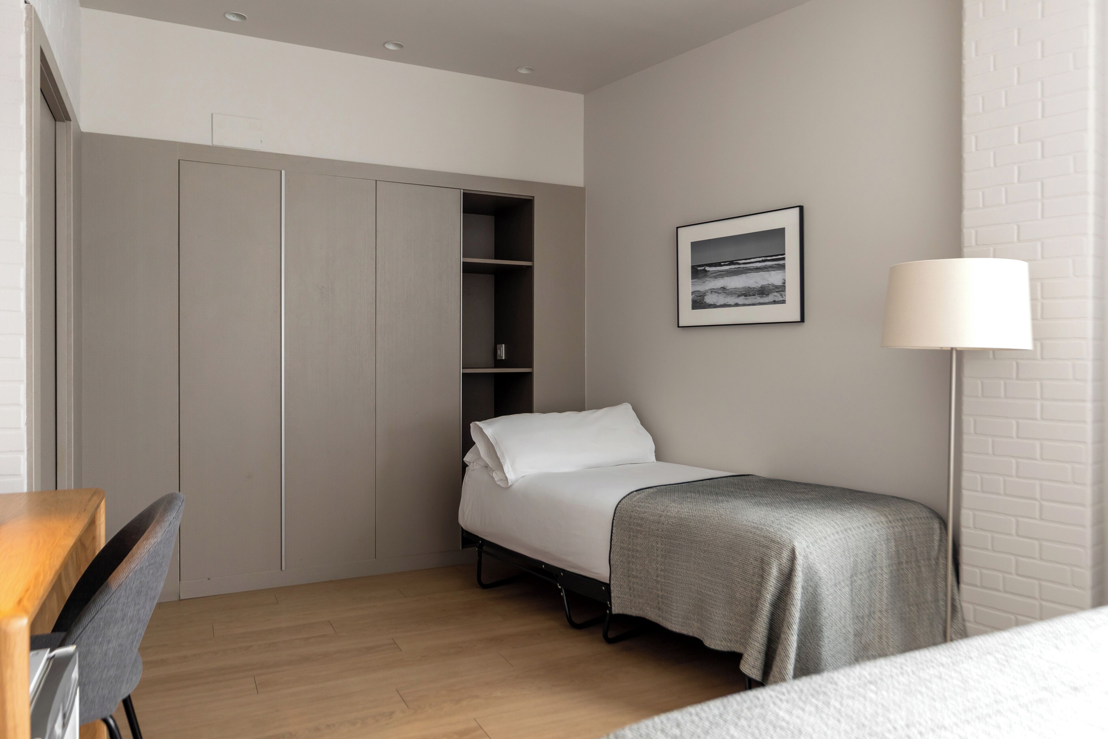 A bedroom with a bed, a desk, a chair, a wardrobe, and a lamp.