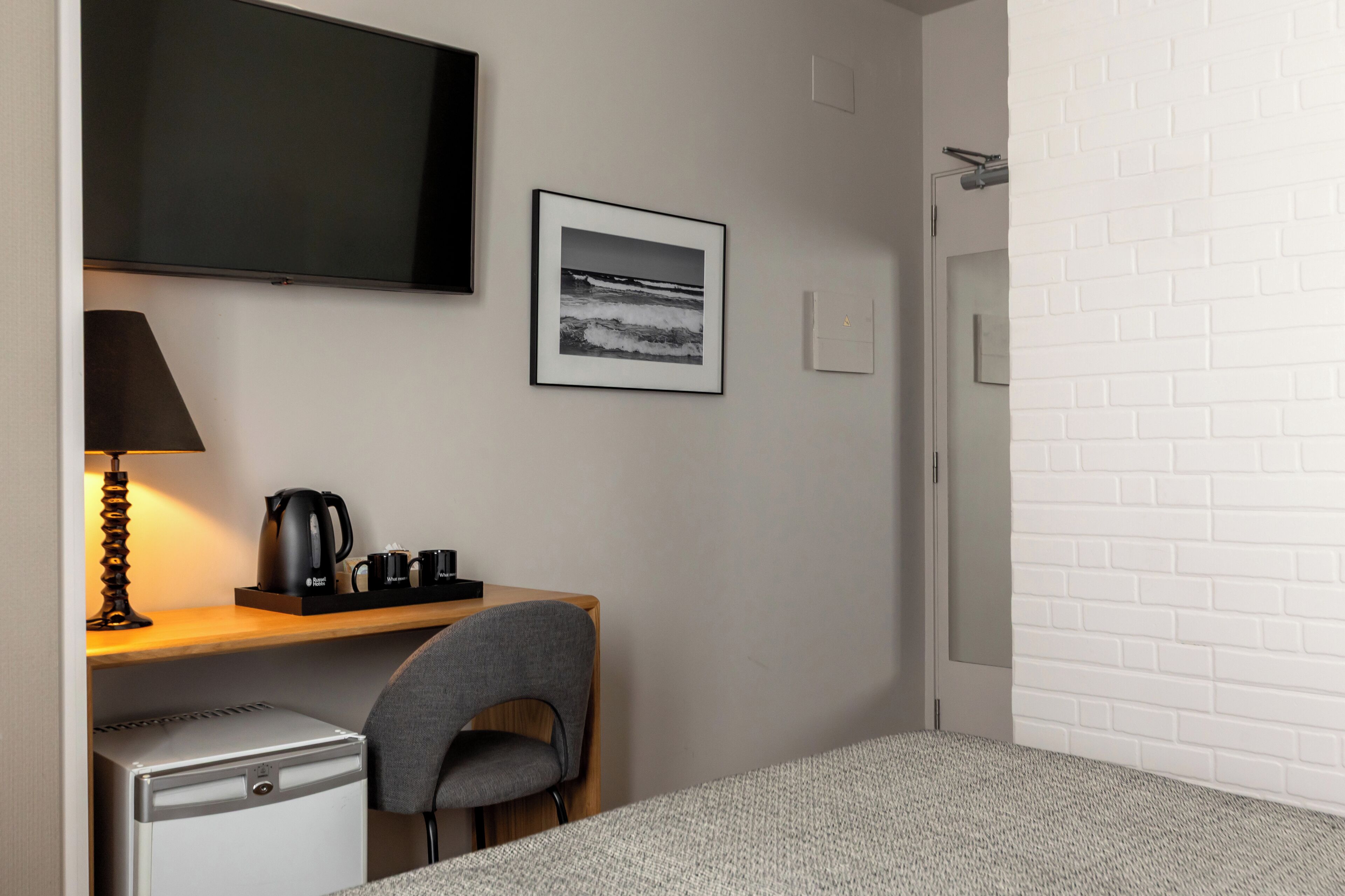 A hotel room with a bed, a desk with a chair, a television, a coffee maker, and a framed picture on the wall.