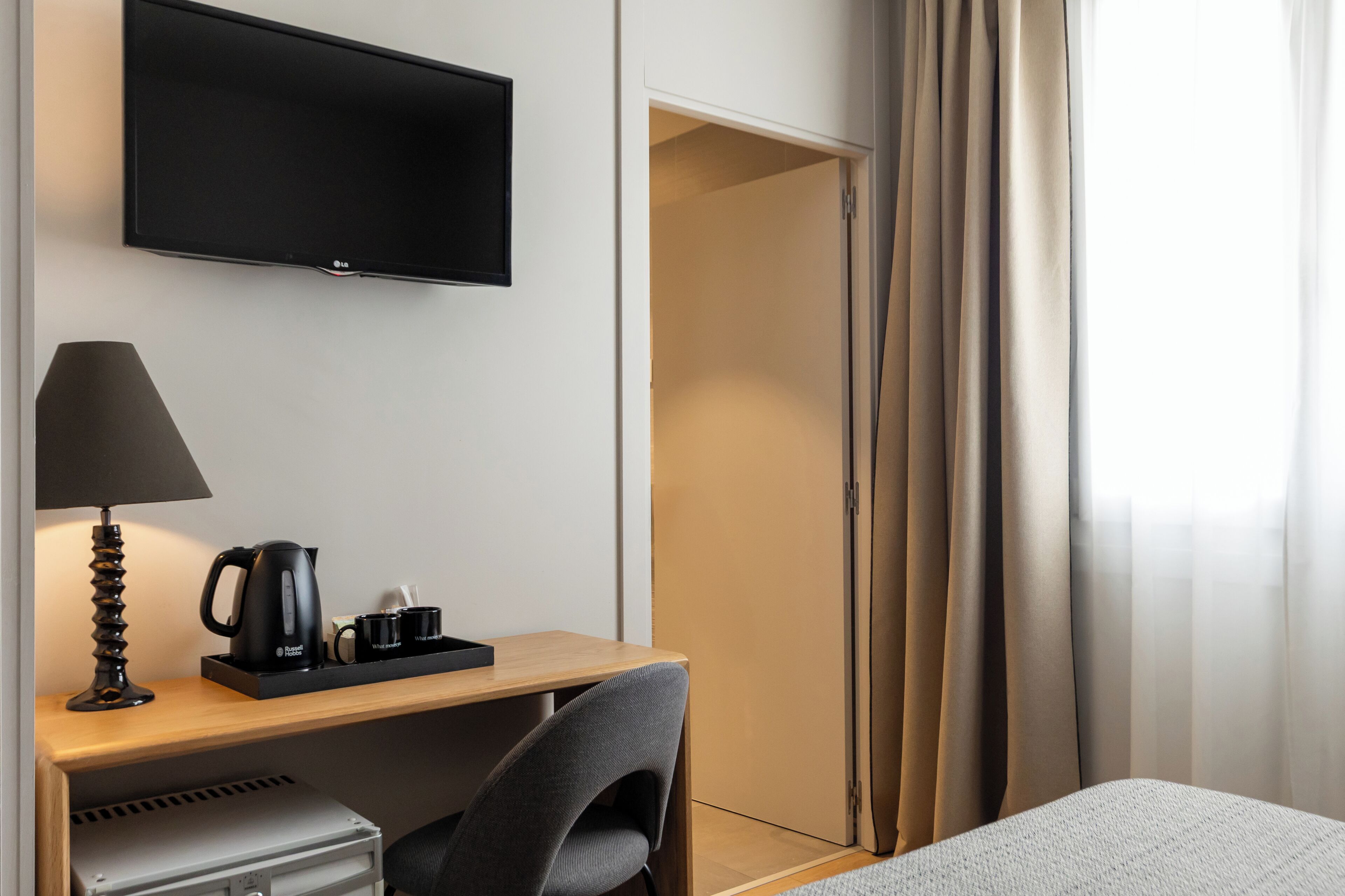 Une chambre d’hôtel équipée d’une télévision à écran plat, d’un bureau avec une lampe, d’une machine à café et d’une chaise.