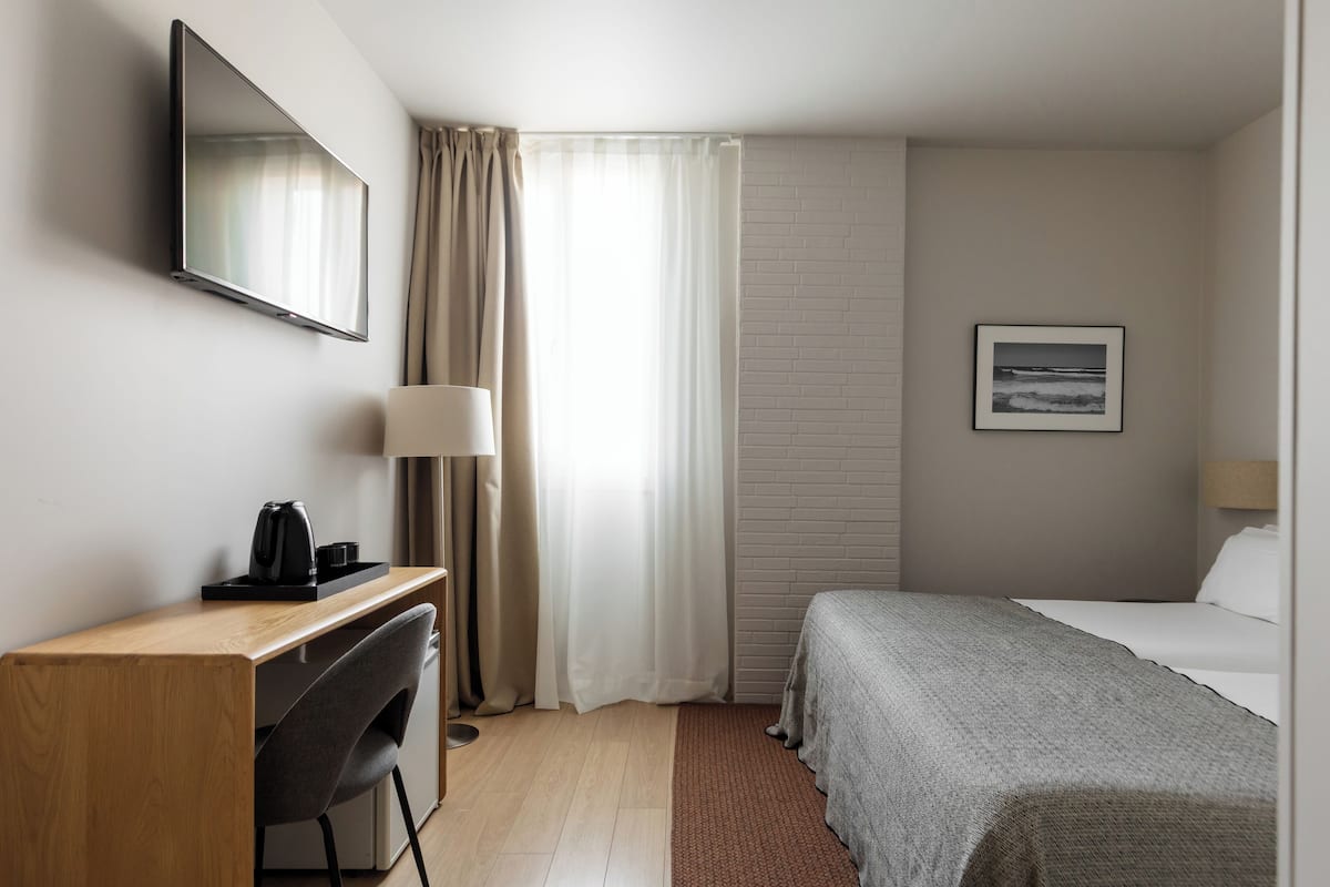 A hotel room with a bed, desk, chair, lamp, and a picture on the wall.