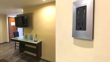 A hotel room with a wooden table, a flat-screen TV mounted on the wall, and a built-in electrical outlet.