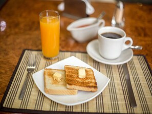 Desayuno con tostadas, mantequilla, un vaso de jugo de naranja, una taza de café y un tazón de sopa sobre una mesa.