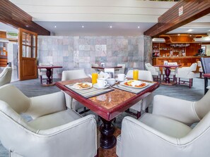Comedor de hotel con paredes de mármol, vigas de madera y un bar al fondo.