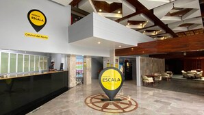 Un hall d'hôtel comprenant un comptoir d'accueil, une grande enseigne indiquant le nom de l'hôtel, et un espace détente avec des tables et des chaises.