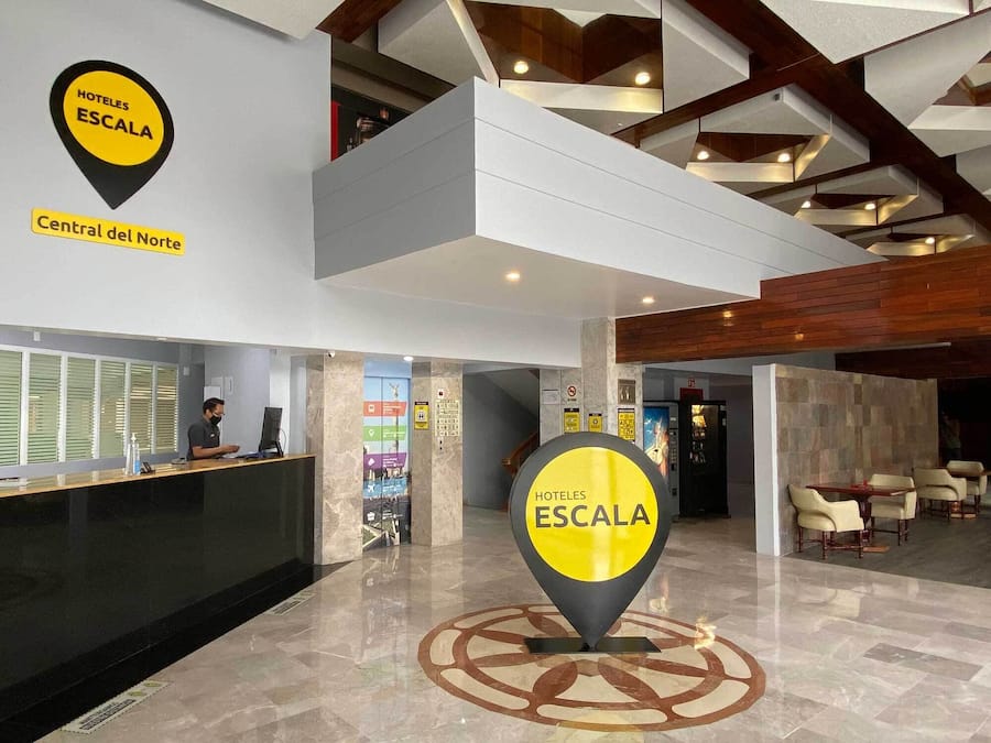 A hotel lobby with a reception desk, a large hotel sign, and a seating area with tables and chairs.