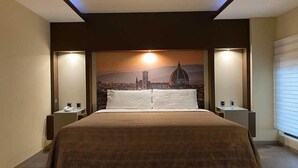 Une chambre d’hôtel avec un grand lit, deux tables de chevet, une petite table et une fresque représentant un paysage urbain sur le mur.