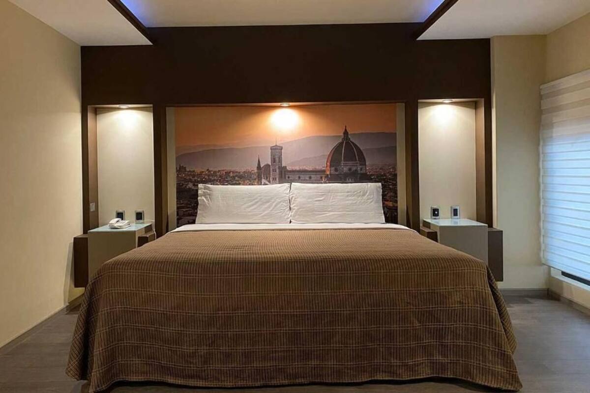 Habitación de hotel con una cama grande, dos mesitas de noche y un mural de paisaje urbano en la pared.