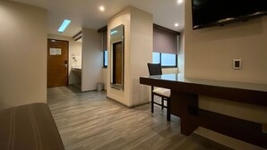 Une chambre d’hôtel moderne avec un banc en bois, un téléviseur fixé au mur et une fenêtre laissant entrer la lumière naturelle.