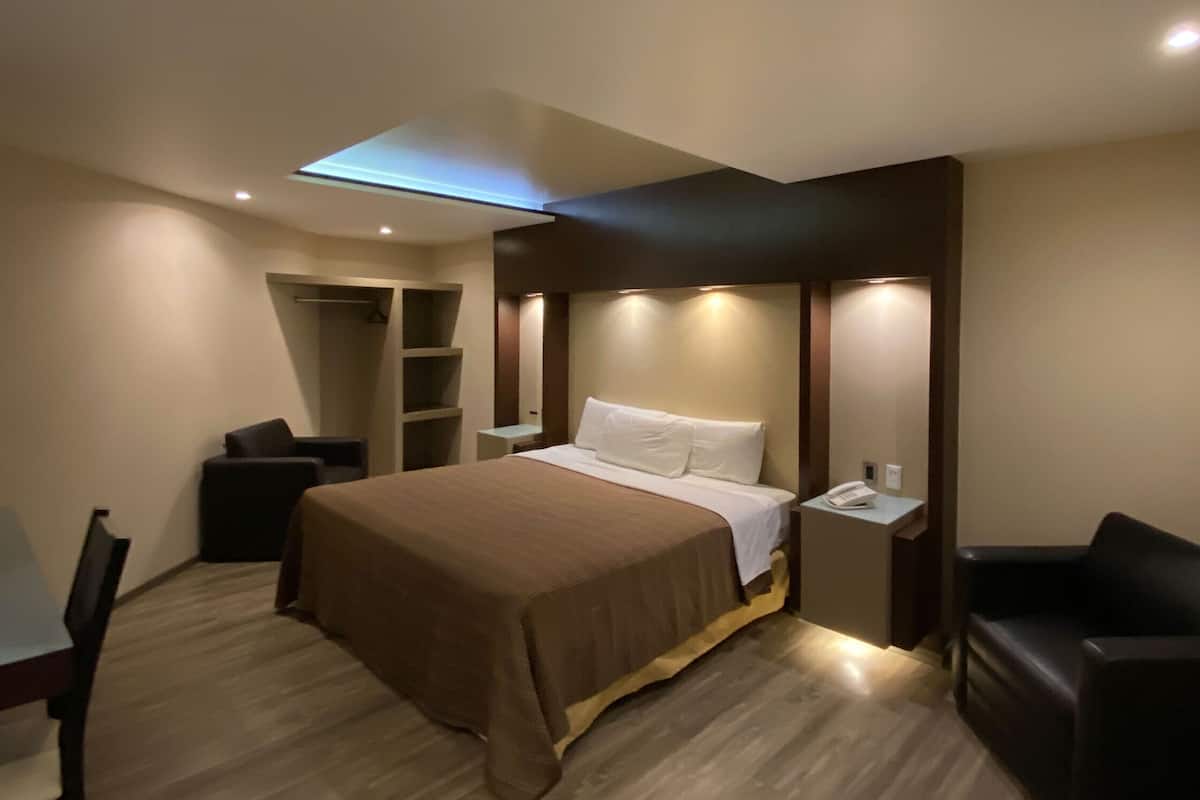 Una habitación de hotel moderna con cama, mesita de noche, silla y estanterías integradas.