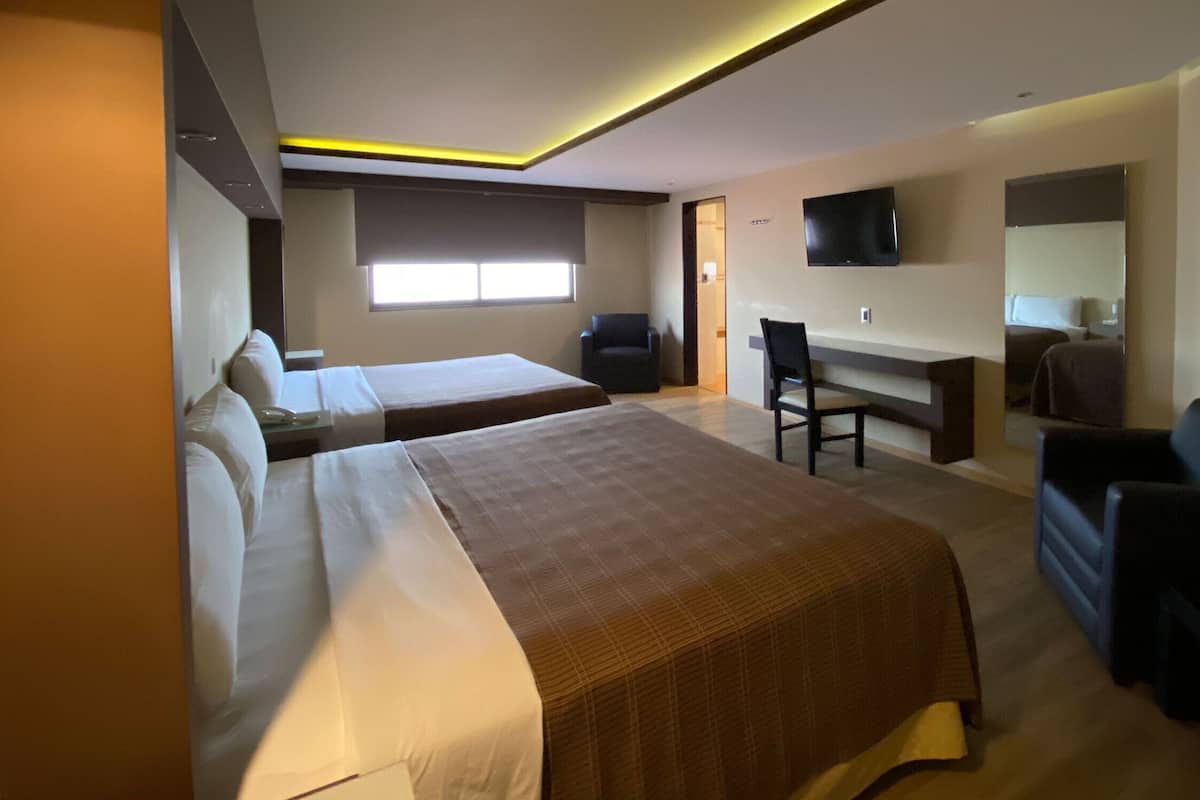 Una habitación de hotel con dos camas, un escritorio, una silla, un televisor y una ventana.