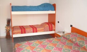 Un lit superposé avec un matelas bleu sur le lit du haut et une couverture matelassée aux couleurs vives sur le lit du bas.