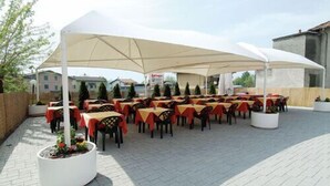 An outdoor dining area with tables covered by large white umbrellas, arranged in rows with chairs. - Colombo Residence (Sorico)