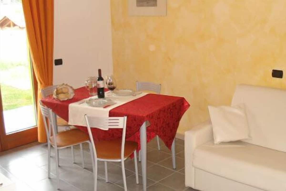 A dining area with a table set for two, a white couch, and a yellow wall.